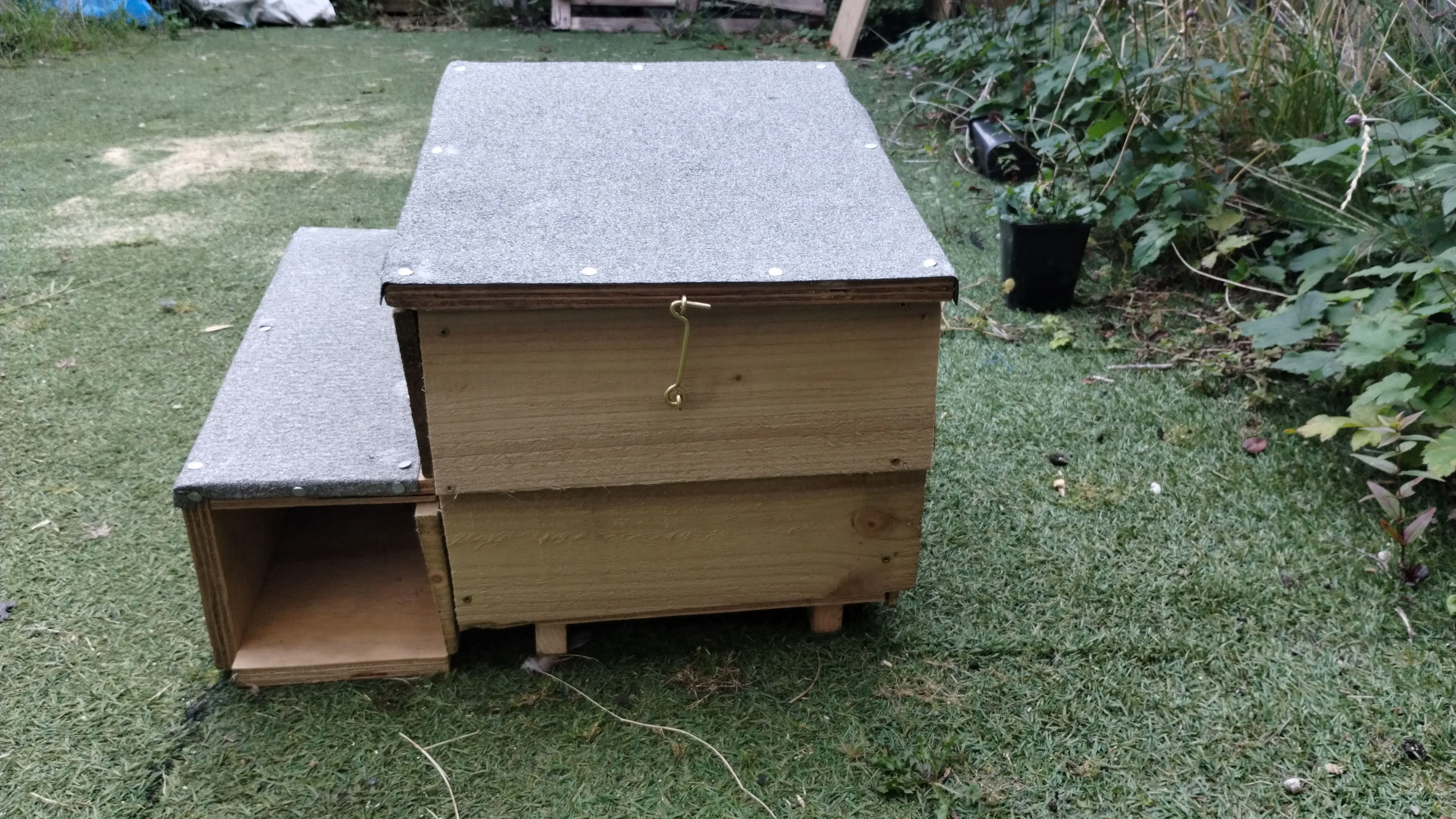 A beehive in a yard with a little bit of grass on the ground.